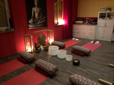 Massageklang - Klangmeditationen von Katrin Leutbecher. Es liegen Yogamatten mit Decken und Kissen auf dem Boden vor einem Gong und Klangschalen.