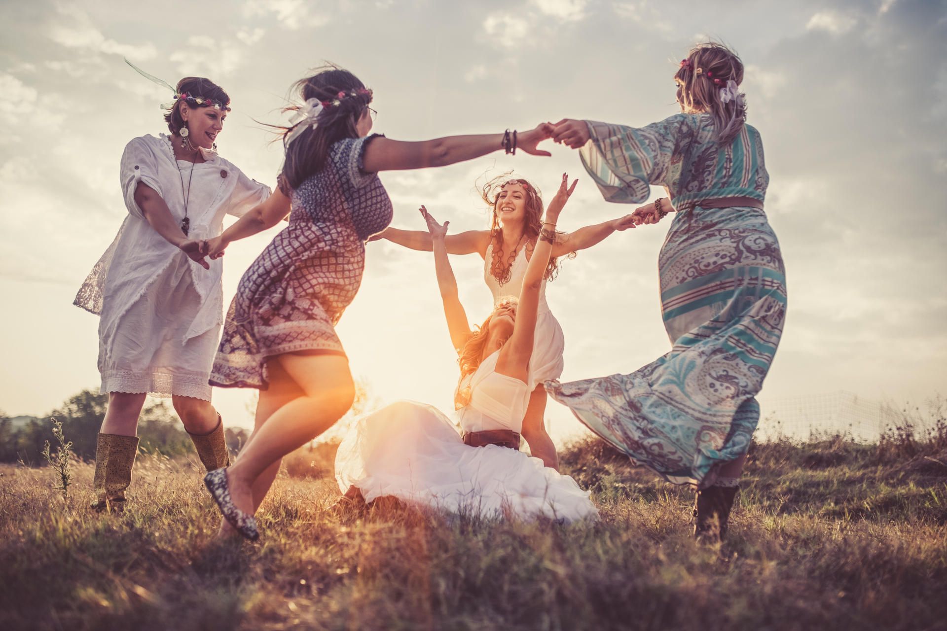 Frauen tanzen vergnügt auf einer Wiese im Kreis - sie feiern ein Jahreskreisfest und fassen sich dabei an die Hände